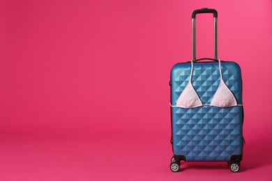 Stylish suitcase with bikini top on color background. Space for text