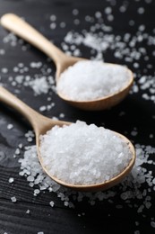 Photo of Organic salt in spoons on black wooden table, closeup