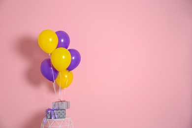 Photo of Bunch of bright balloons and gifts on table against color wall. Space for text