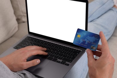 Man with credit card using laptop for online shopping on sofa, closeup