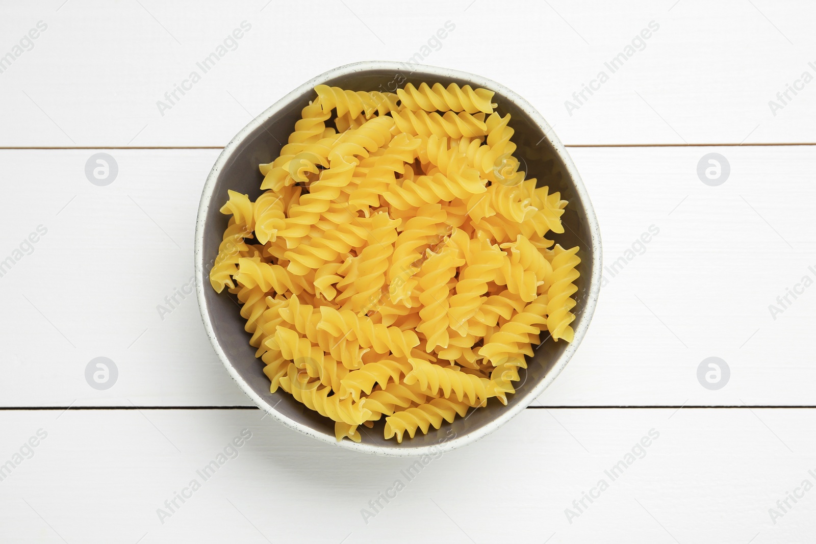 Photo of Raw fusilli pasta in bowl on white wooden table, top view