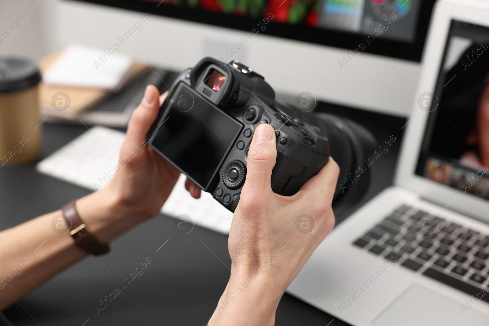 Photo of Professional photographer with digital camera at table indoors, closeup