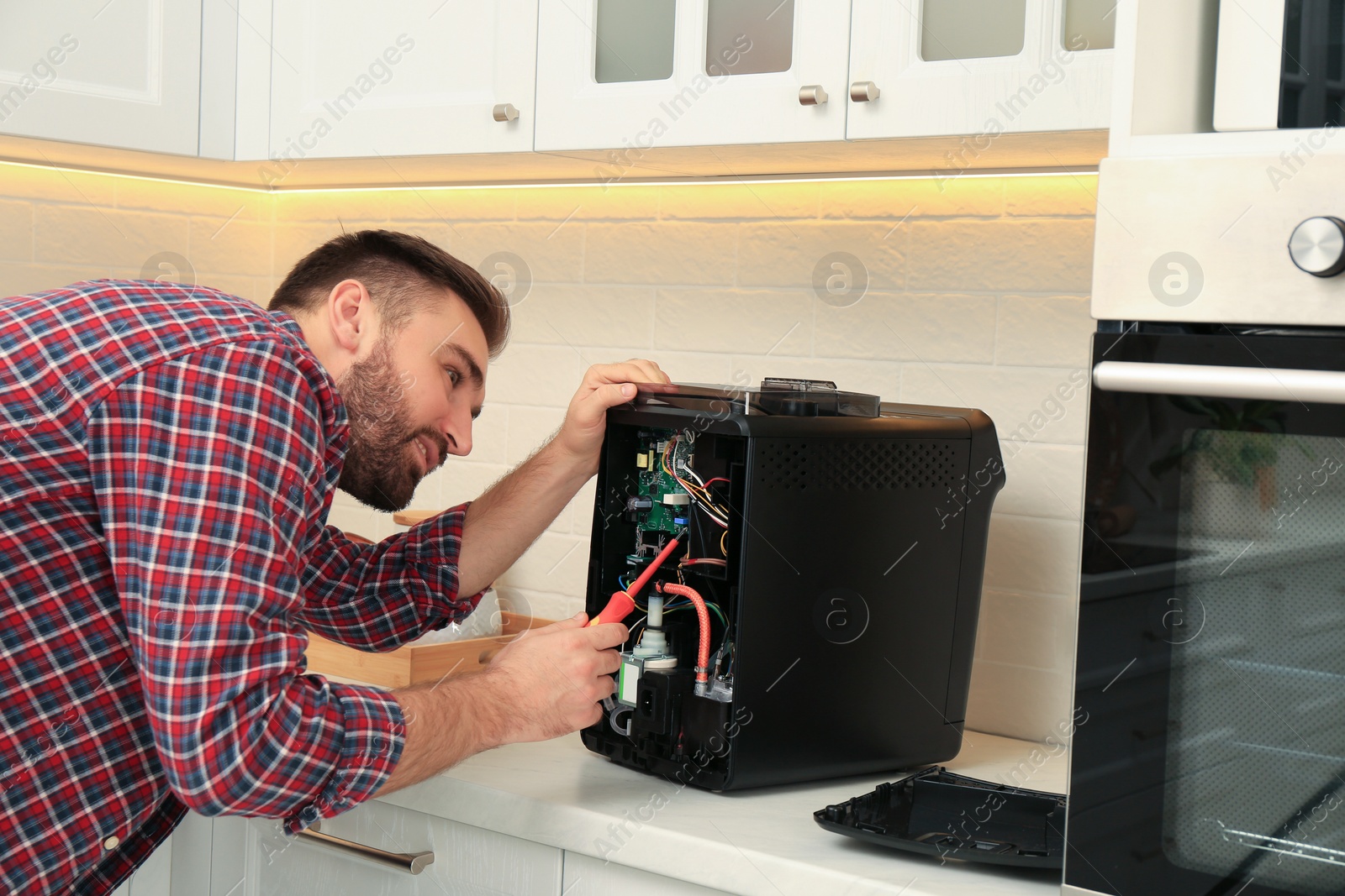 Photo of Man with screwdriver fixing coffee machine at table in kitchen