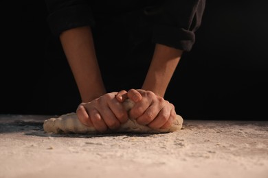 Photo of Making bread. Woman kneading dough at table on dark background, closeup