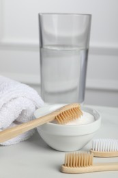 Bamboo toothbrushes, bowl of baking soda, towel and glass of water on white table