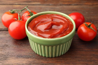 Photo of Bowl of tasty ketchup and tomatoes on wooden table, closeup