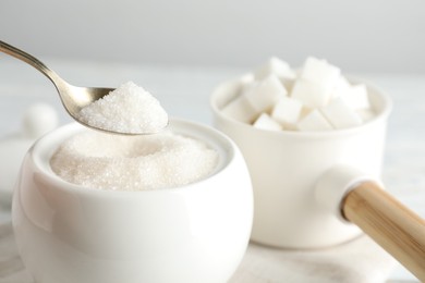 Taking spoon of white sugar from ceramic bowl on table, closeup
