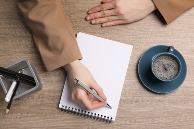 Woman writing in notebook at wooden table, top view