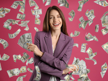 Happy young woman with dollars under money rain on pink background