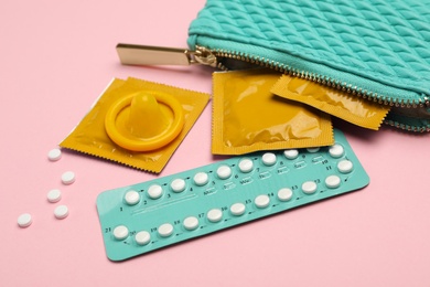 Photo of Purse with condoms and birth control pills on pink background. Safe sex