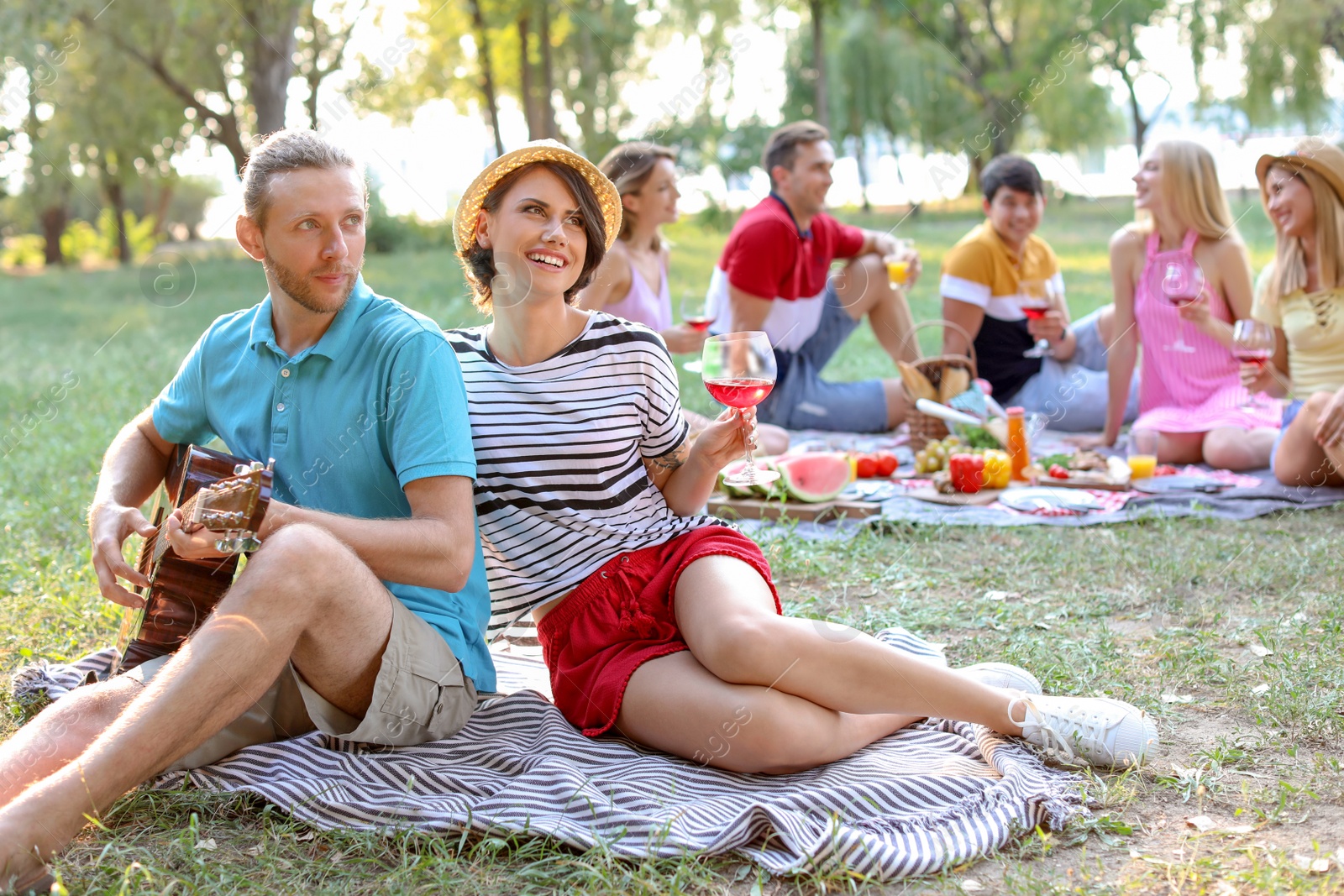 Photo of Young man playing guitar for his girlfriend in park. Summer picnic