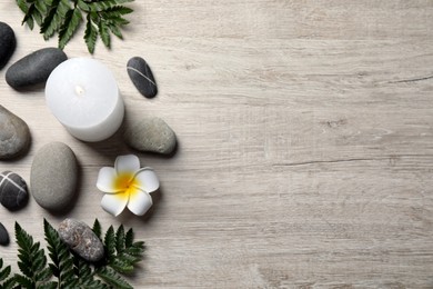 Photo of Burning candle, plumeria flower and spa stones on light beige wooden table, flat lay. Space for text