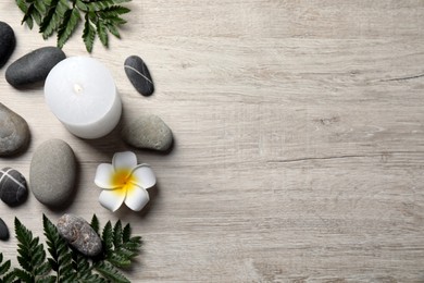 Burning candle, plumeria flower and spa stones on light beige wooden table, flat lay. Space for text