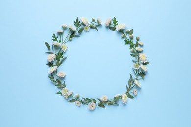 Photo of Wreath made of beautiful flowers and green leaves on light blue background, flat lay. Space for text