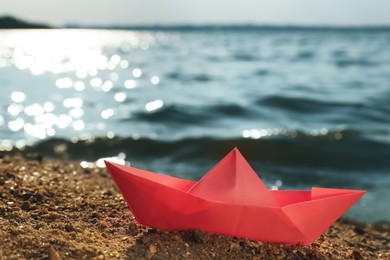 Pink paper boat near river on sunny day