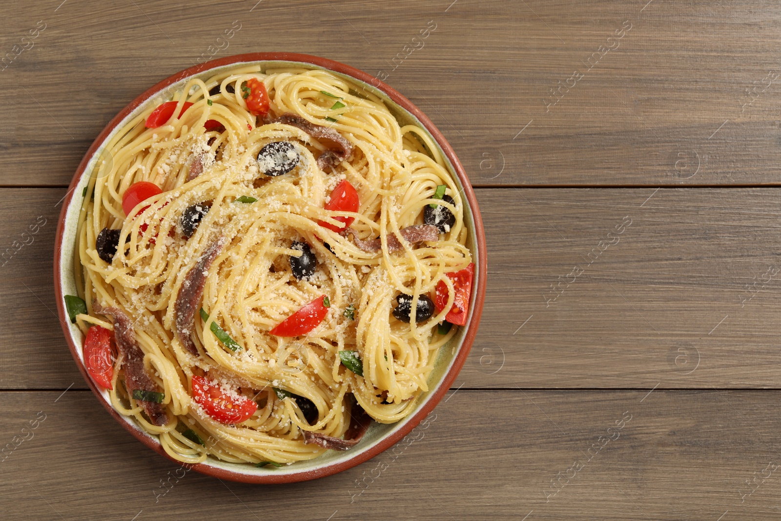 Photo of Plate of delicious pasta with anchovies, tomatoes and parmesan cheese on wooden table, top view. Space for text