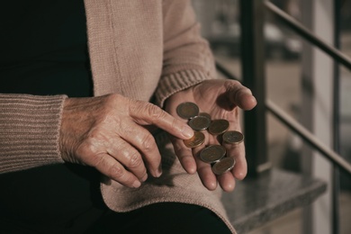 Photo of Poor senior woman with coins on stairs, closeup