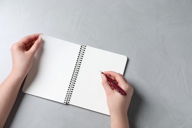 Photo of Woman writing in notebook with pen at light grey table, top view. Space for text