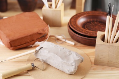 Clay and set of modeling tools on wooden table in workshop