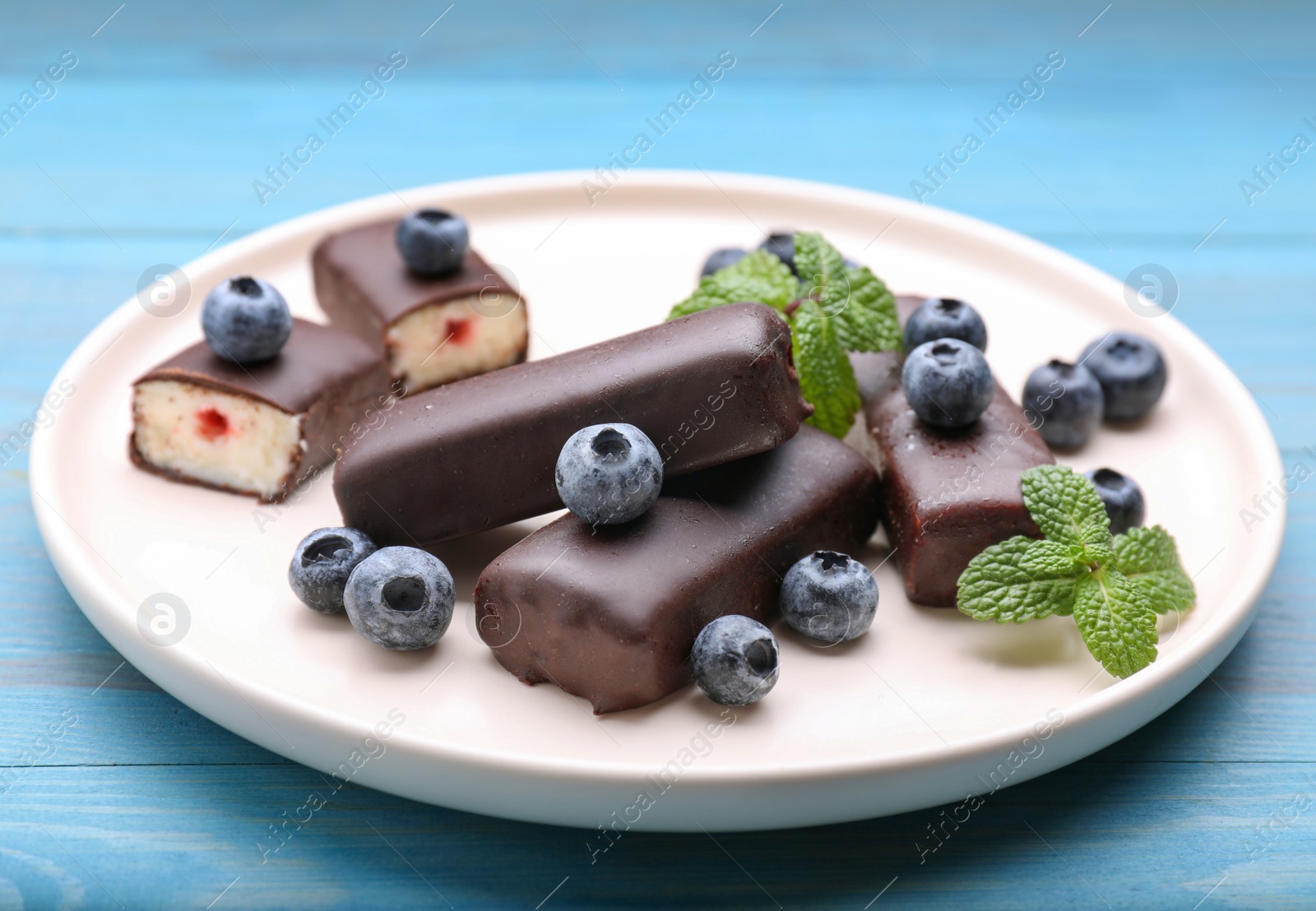 Photo of Delicious glazed curd snacks with fresh blueberries and mint on light blue wooden table