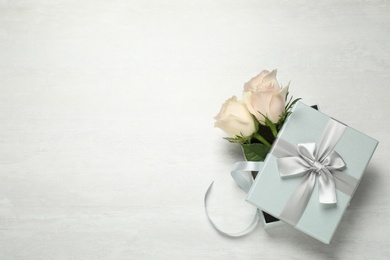 Photo of Elegant gift box with beautiful flowers on white table, top view. Space for text