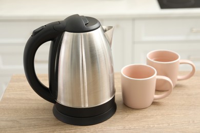 Photo of Modern electric kettle and cups on table in kitchen