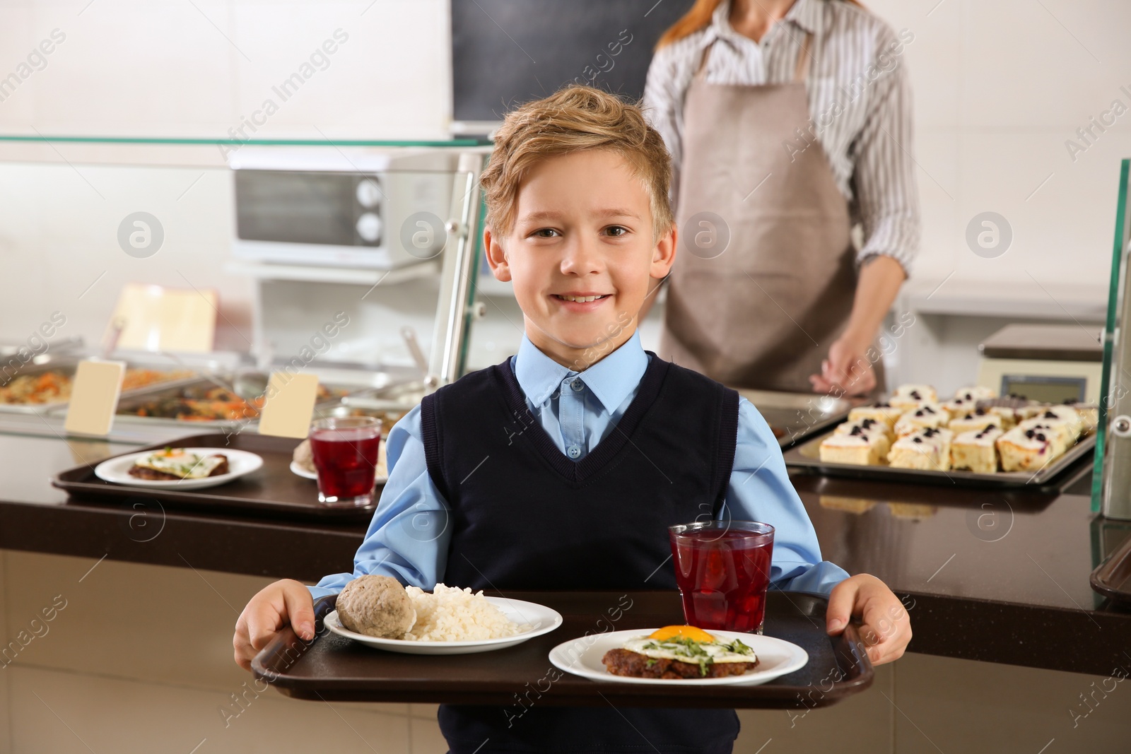 Photo of Cute boy holding tray with healthy food in school canteen