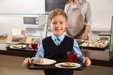 Cute boy holding tray with healthy food in school canteen