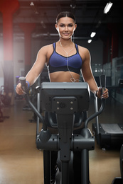 Photo of Young woman working out on elliptical trainer in modern gym