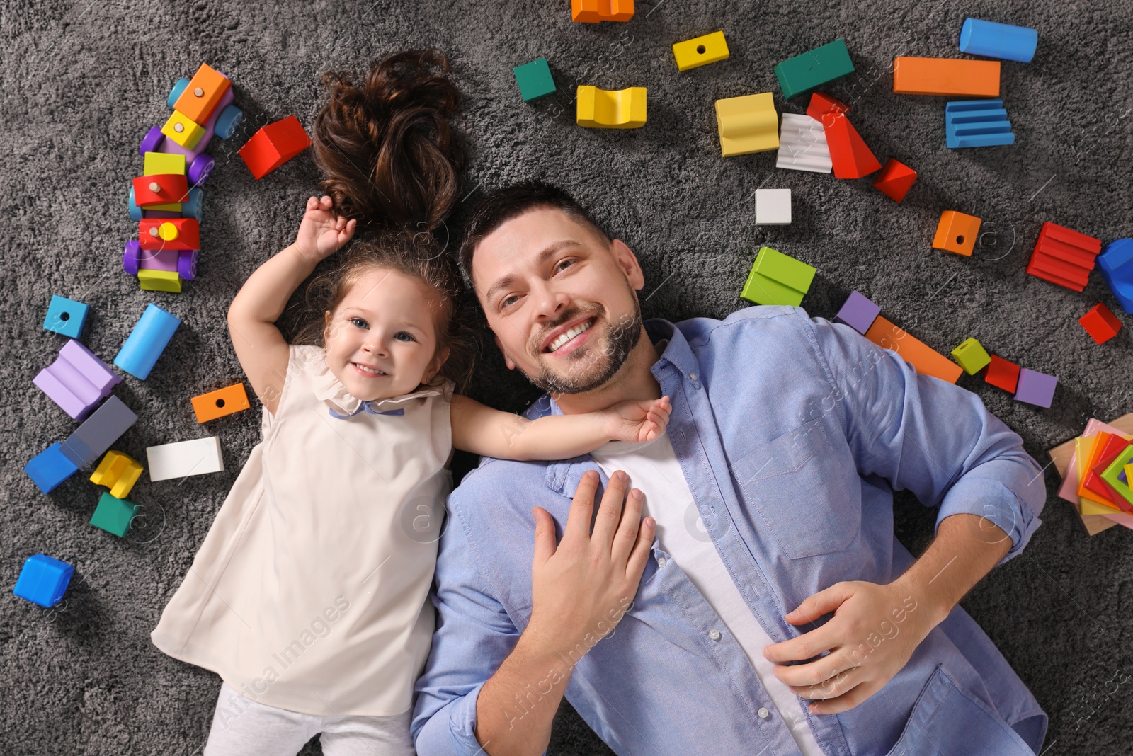 Photo of Father and daughter lying on floor at home, top view. Playing with children