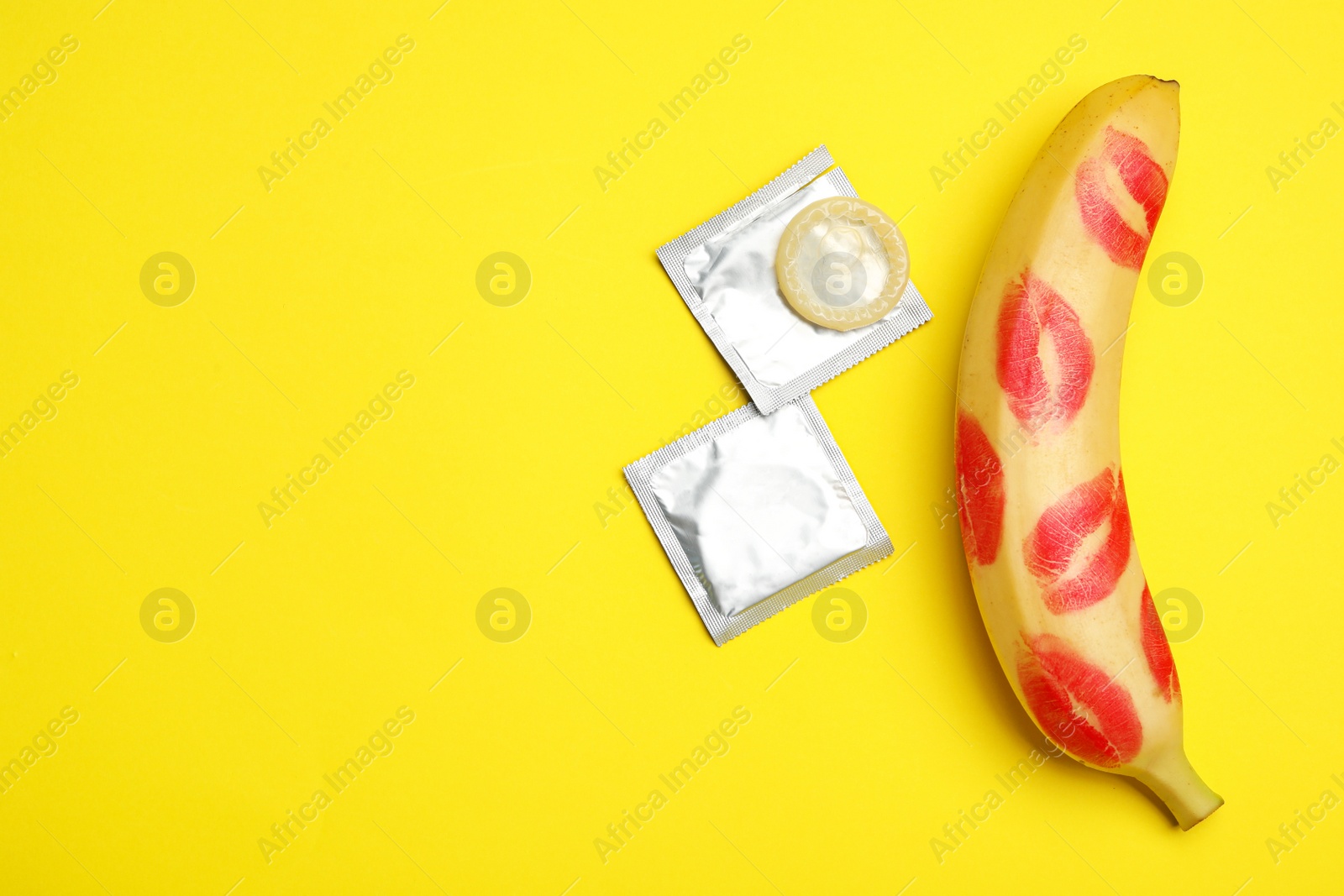 Photo of Condoms, banana with lipstick kiss marks and space for text on yellow background, flat lay. Safe sex