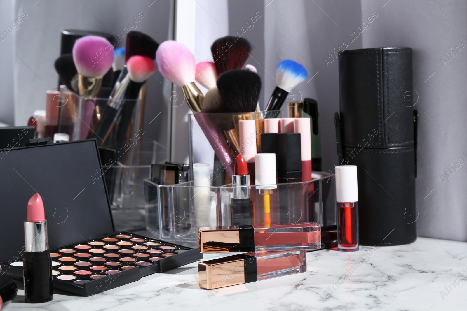 Photo of Bright lip glosses among different cosmetic products on white dressing table