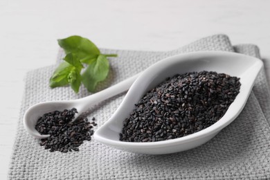 Black sesame seeds and green leaf on white table, closeup