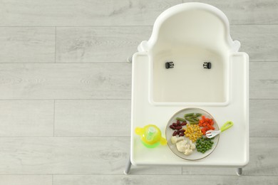 Photo of Baby high chair with healthy food and water, top view. Space for text