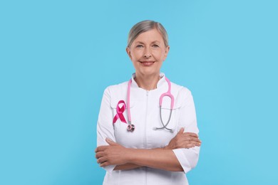 Photo of Doctor with pink ribbon and stethoscope on light blue background. Breast cancer awareness