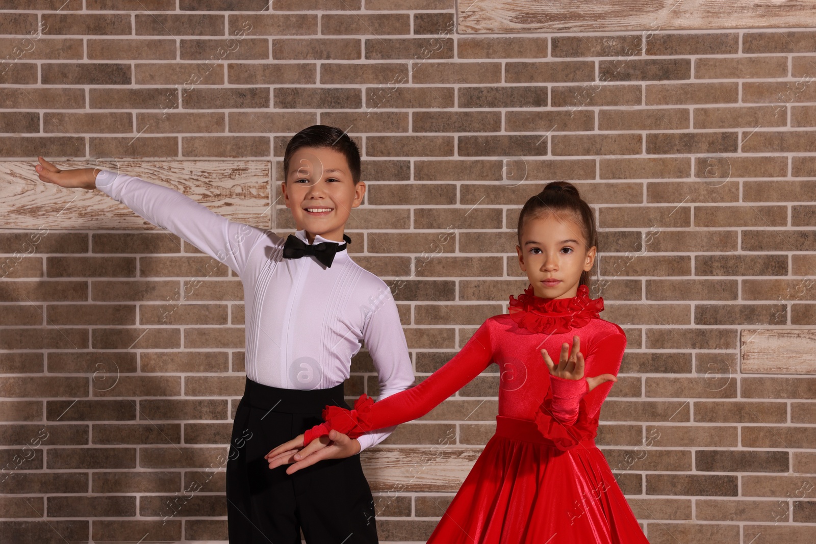 Photo of Beautifully dressed couple of kids dancing together near brick wall indoors