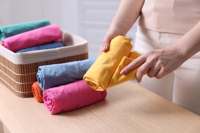 Photo of Woman with rolled shirt near basket at table indoors, closeup. Organizing clothes