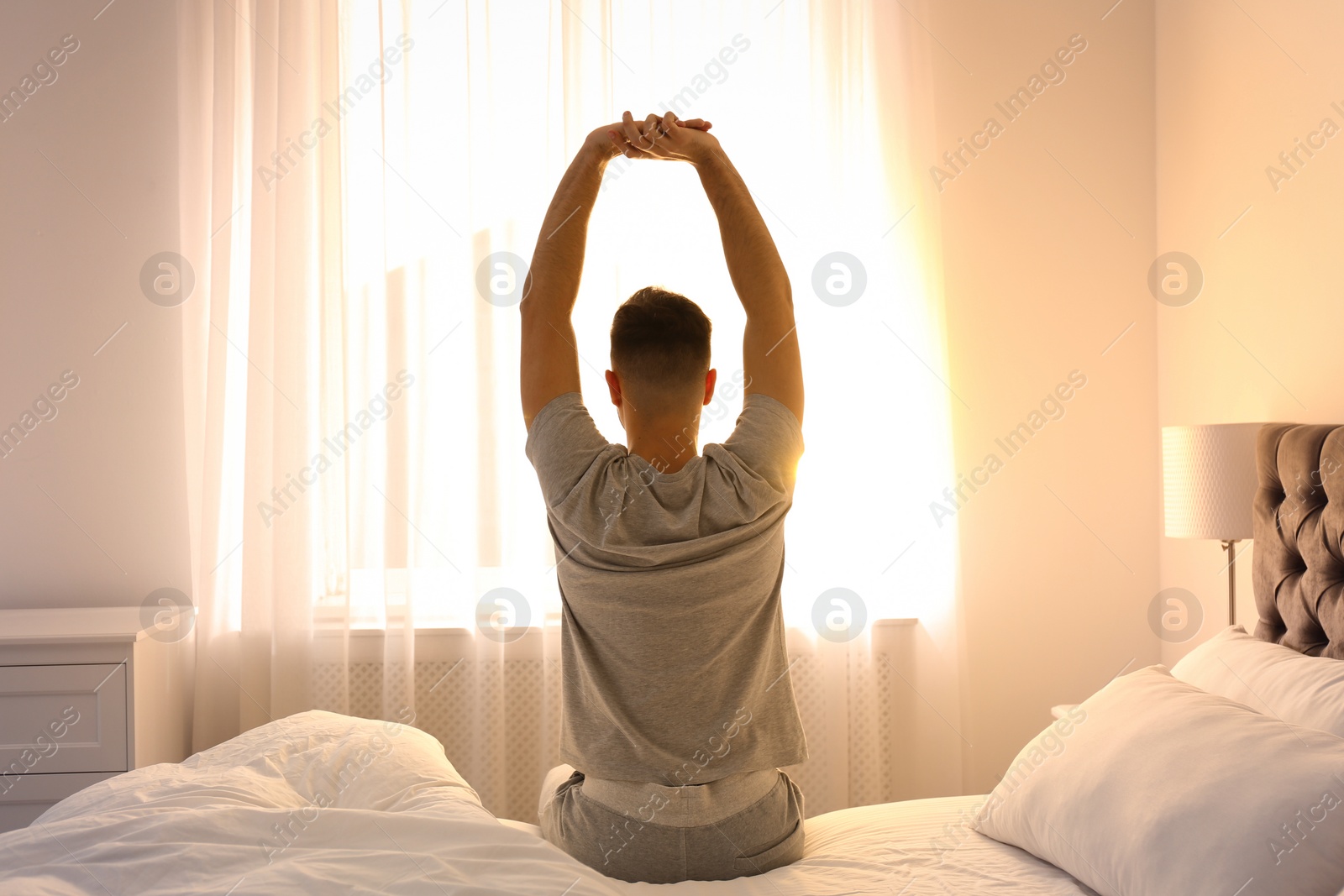 Photo of Young man stretching on bed at home, view from back. Lazy morning