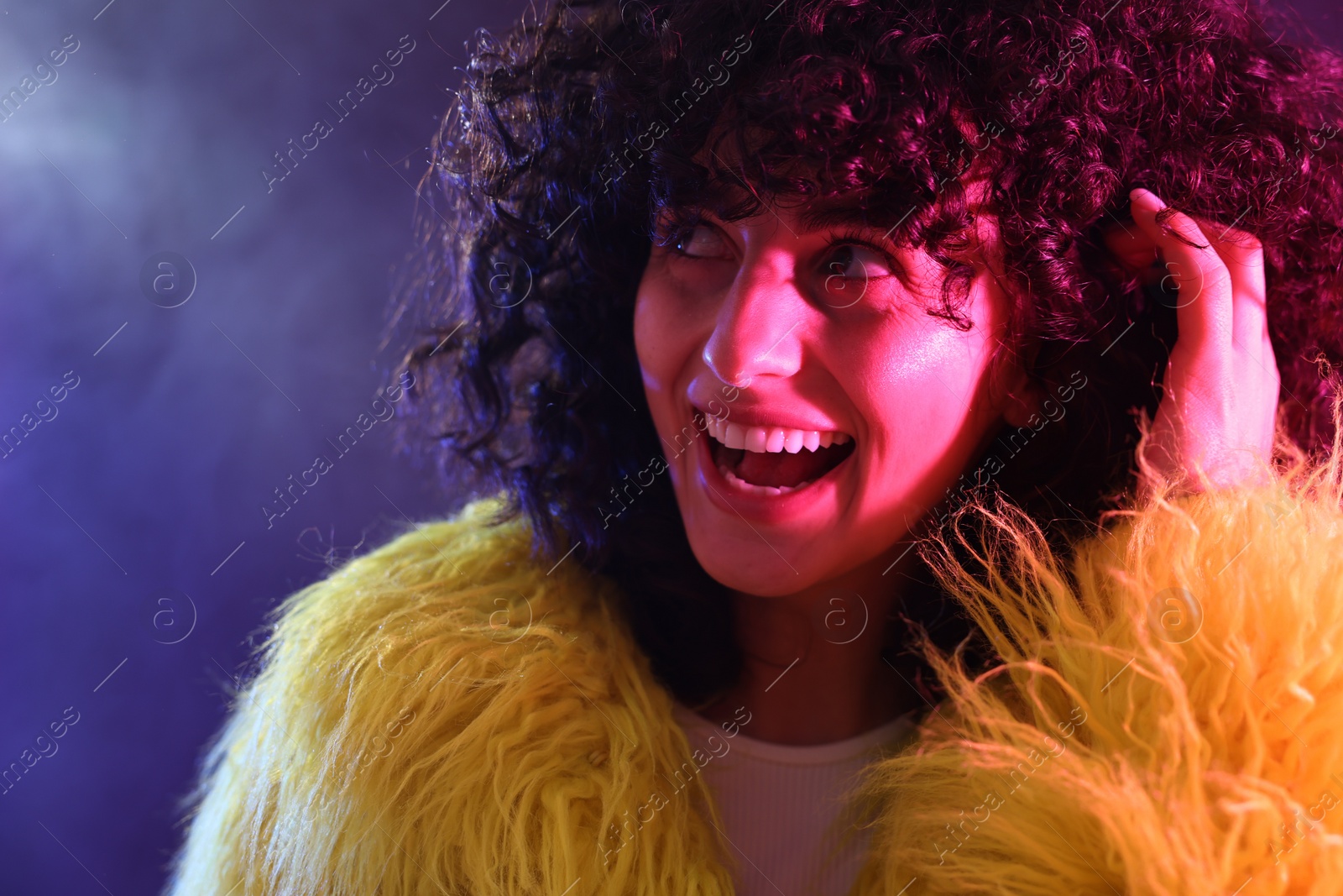 Photo of Beautiful young woman in yellow fur coat on color background in neon lights, closeup