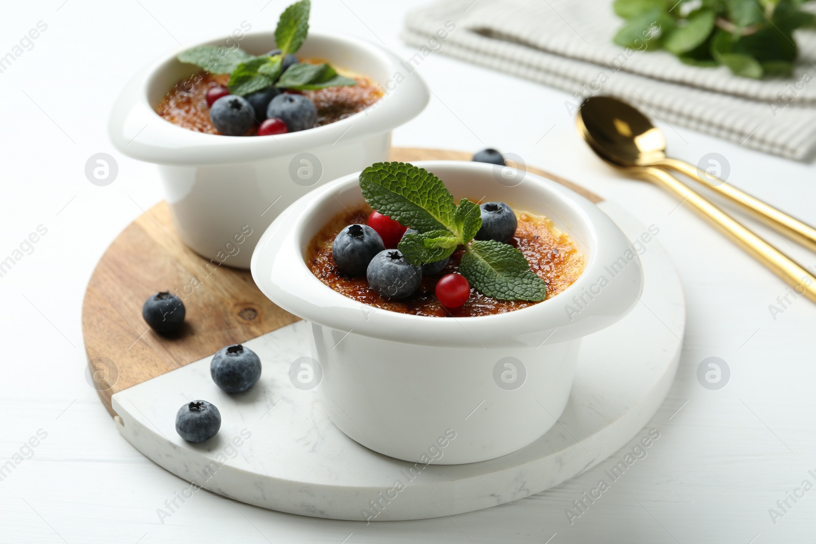 Photo of Delicious creme brulee with berries and mint in bowls on white wooden table, closeup