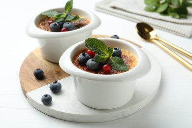 Photo of Delicious creme brulee with berries and mint in bowls on white wooden table, closeup