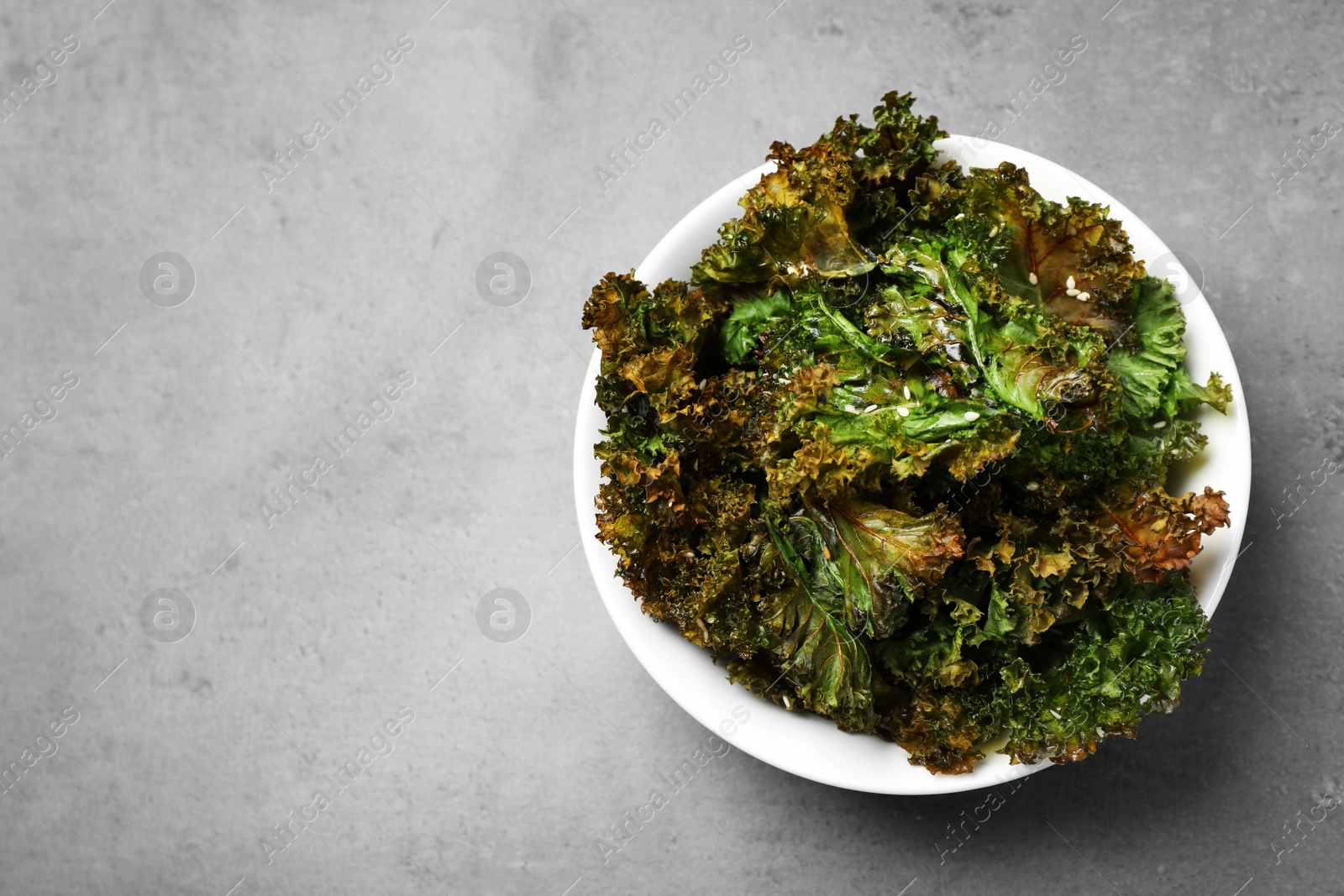 Photo of Tasty kale chips with seeds on grey table, top view. Space for text