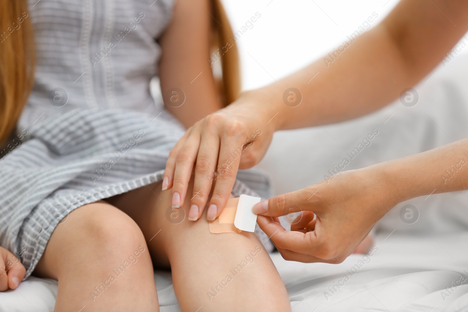 Photo of Woman applying plaster on girl's knee, closeup view