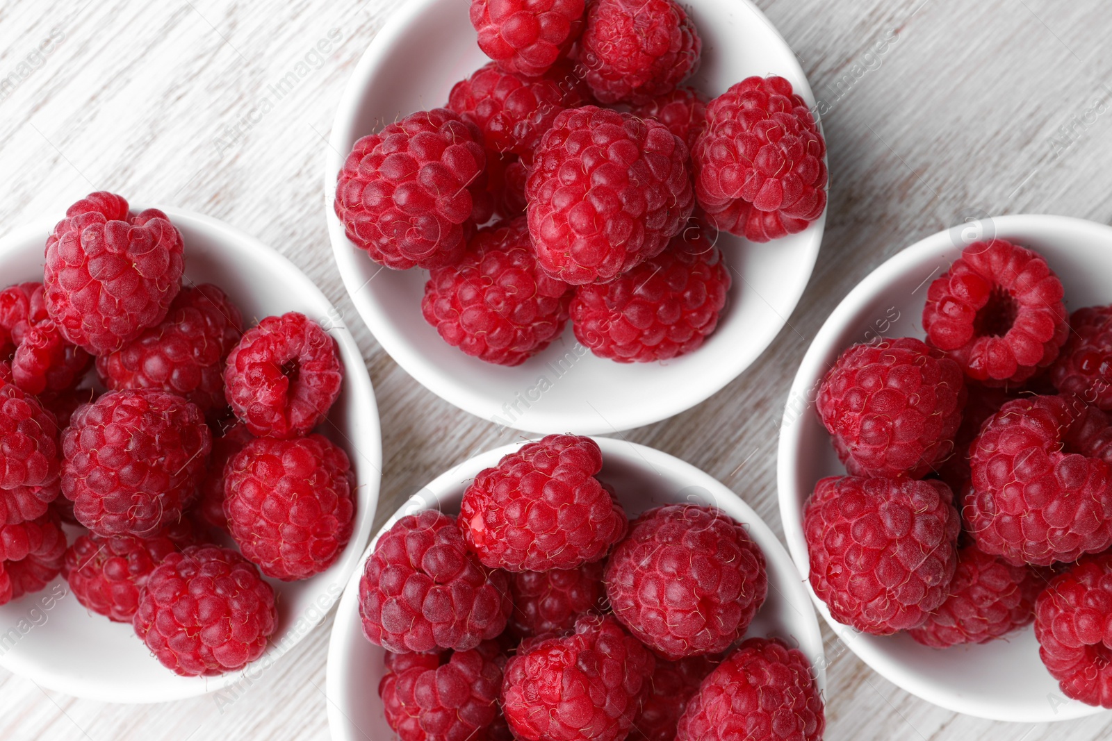 Photo of Tasty ripe raspberries on white wooden table, flat lay