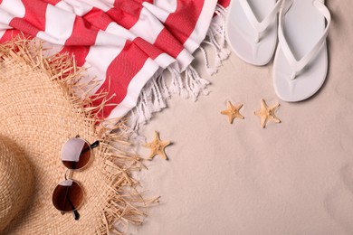 Beach towel, hat, sunglasses, starfishes and flip flops on sand, flat lay