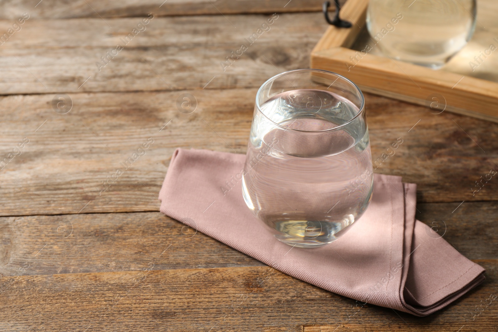 Photo of Glass of water and napkin on wooden table. Space for text