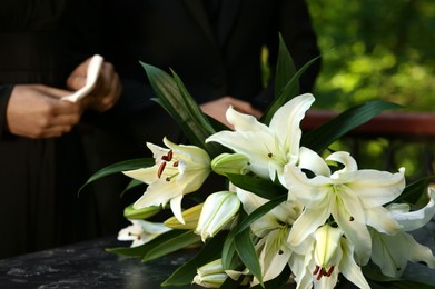 Photo of People near white lilies on granite tombstone at cemetery outdoors, closeup. Funeral ceremony