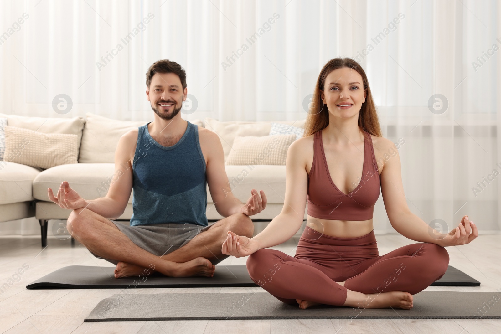 Photo of Couple in sportswear meditating together at home. Harmony and zen