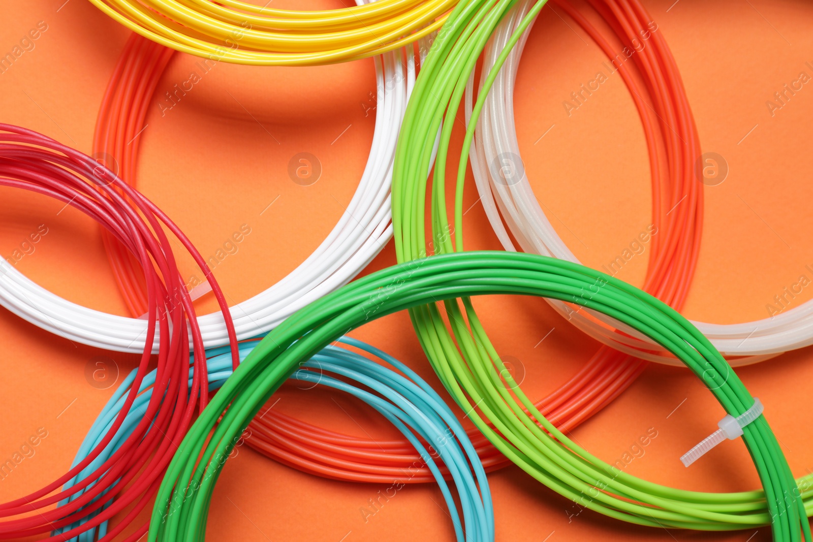 Photo of Colorful plastic filaments on orange background, flat lay