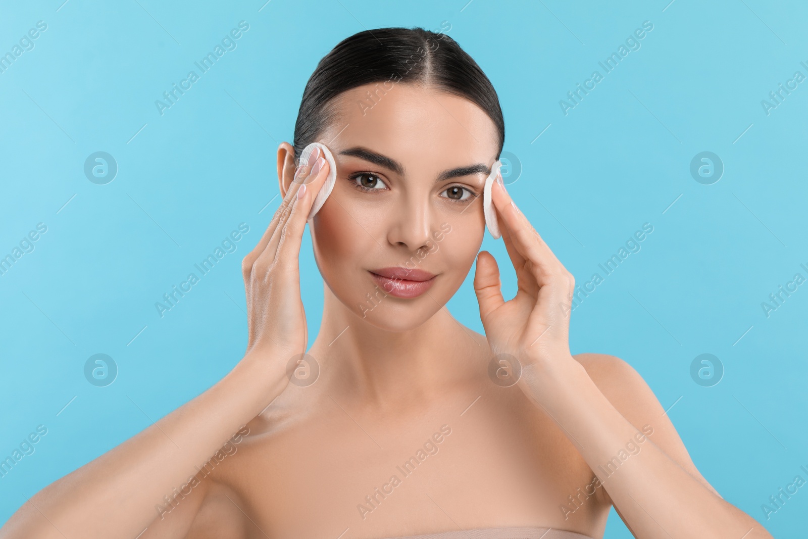 Photo of Beautiful woman removing makeup with cotton pads on light blue background